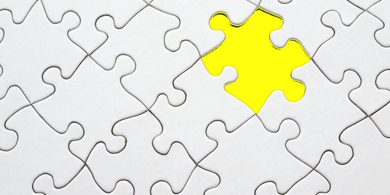 A top-down perspective of a plain grey puzzle with a missing piece highlighted in a bright yellow.